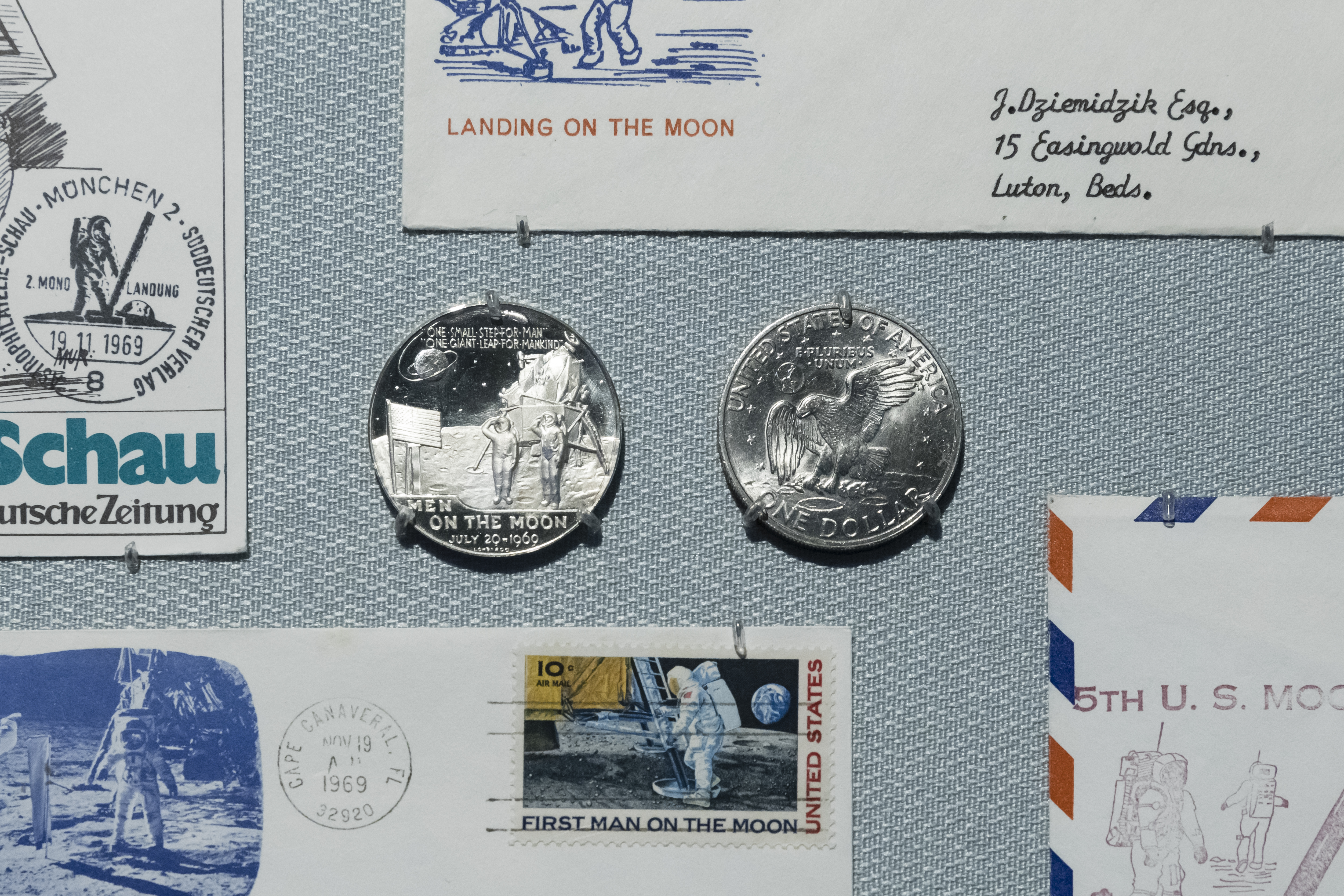 Two small silver medallions, surrounded by commemorative envelopes, all bearing imagery from the Apollo 11 mission.